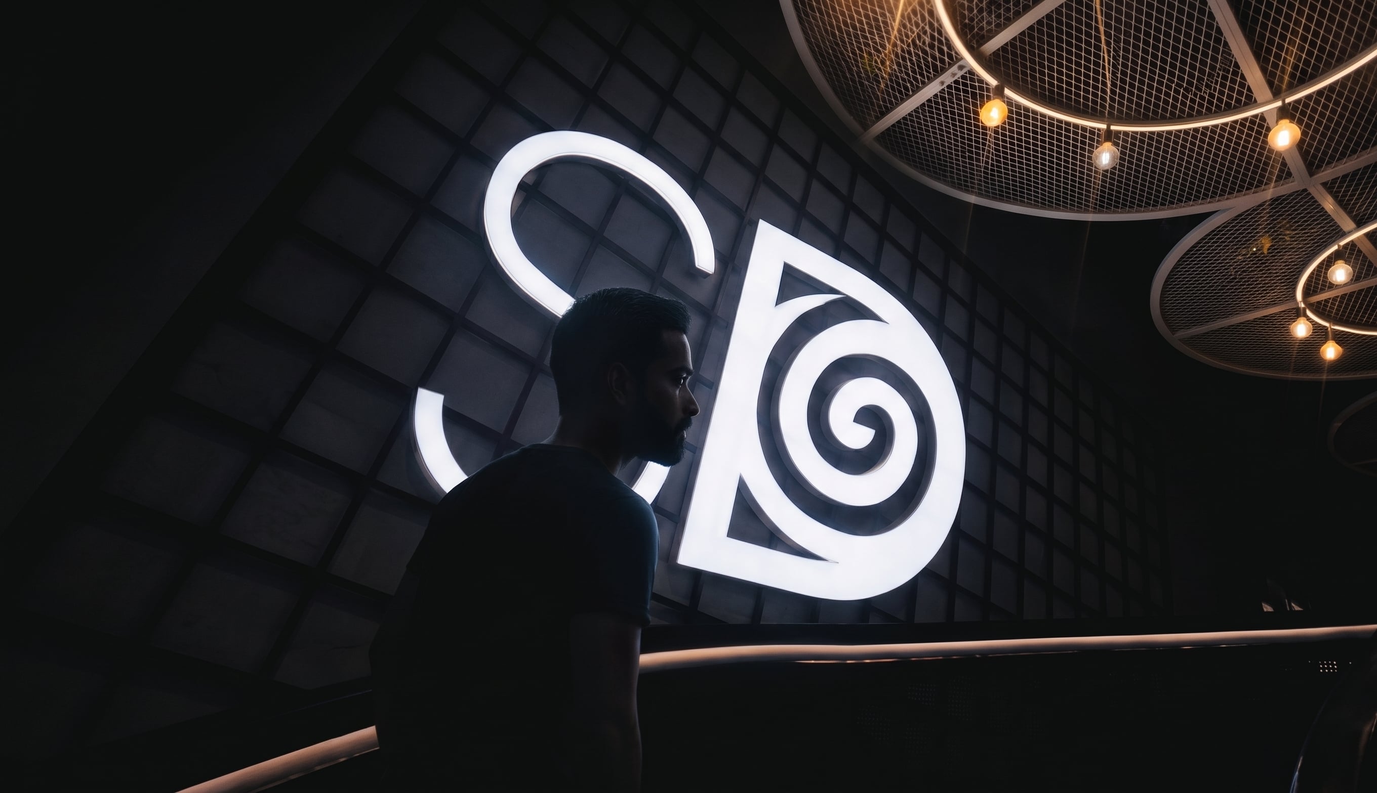 Profile of the Scroll Deeper CEO standing in a dimly lit room in front of a glowing, massive SD neon logo, representing the forward-thinking vision of the Gen AI and Agentic AI agency.